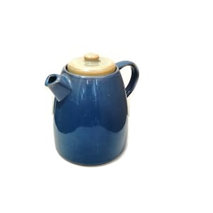 Op de afbeelding: Een blauwe koffiekan van keramiek met een lichtbruin deksel. De kan heeft een rond lichaam en een tuit aan de zijkant.