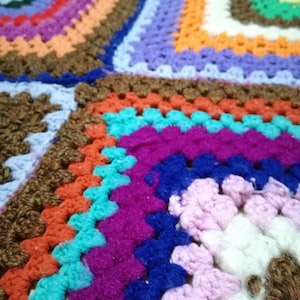 Puede incluir: Una manta de crochet colorida con cuadrados de diferentes colores, incluyendo rojo, naranja, amarillo, verde, azul, morado y marrón.