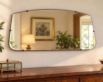 May include: A horizontal wall mirror with a curved top edge and a thin black metal frame. The mirror is secured by small, dark circular fasteners along the perimeter, creating a clean and simple design that reflects the surrounding room interior.