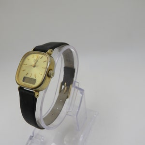 K&ouml;nnte beinhalten: Eine goldfarbene Armbanduhr mit quadratischem Zifferblatt und schwarzem Lederarmband. Die Uhr verf&uuml;gt &uuml;ber ein digitales Display und analoge Zeiger.