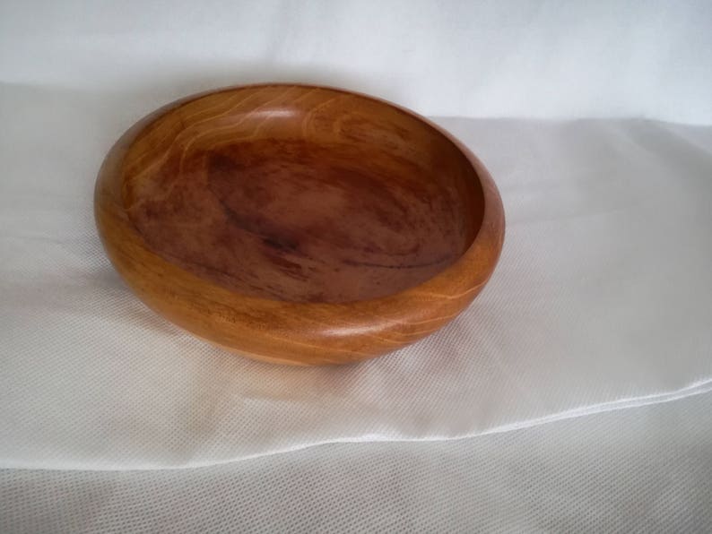 K&ouml;nnte beinhalten: Eine Holzschale mit nat&uuml;rlicher brauner Oberfl&auml;che. Die Schale ist rund und hat eine leichte W&ouml;lbung an den Seiten. Sie ist aus einem einzigen St&uuml;ck Holz gefertigt und hat eine glatte, polierte Oberfl&auml;che.