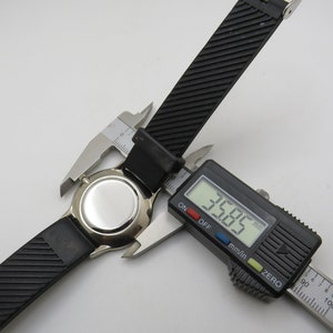 May include: A black watch strap with a silver watch face is being measured with a digital caliper. The caliper reads 35.85 mm.