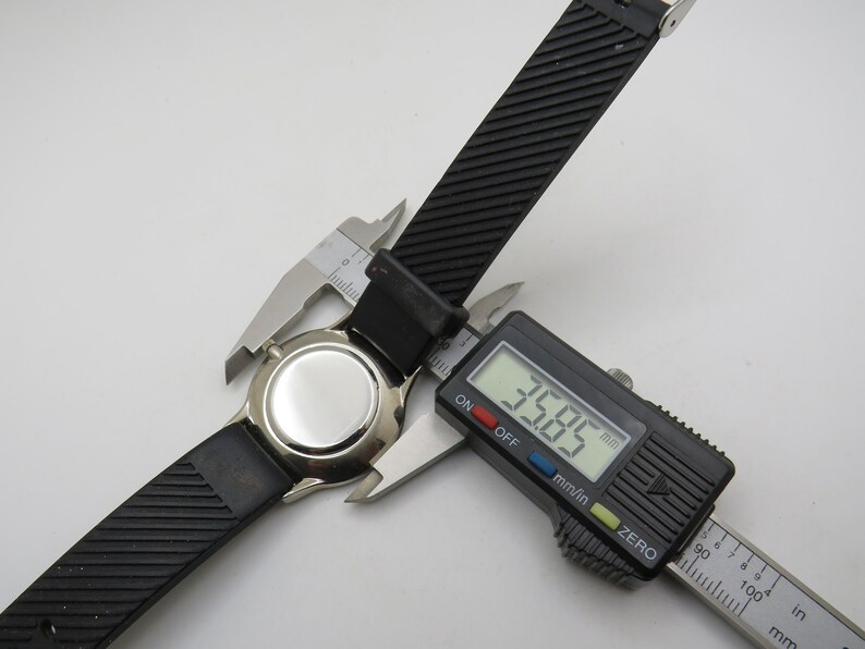 May include: A black watch strap with a silver watch face is being measured with a digital caliper. The caliper reads 35.85 mm.