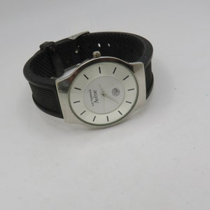 May include: A silver wristwatch with a white face and black rubber band. The watch face has black markings and the word "Avene" printed on it.