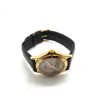 May include: A gold-tone wristwatch with a black leather band. The watch face has a white background with a floral design and Roman numeral hour markers. The watch face also has the word "Zodiac" printed on it.