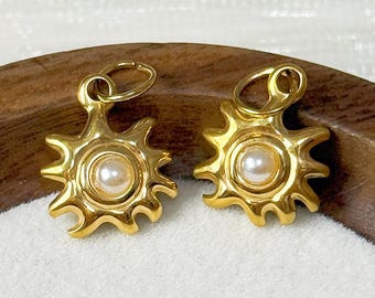May include: A pair of gold-colored earrings with a sunburst design, each featuring a central pearl. The earrings are displayed on a wooden tray with a white interior. The text "@SantomaroDesign" is visible at the top.