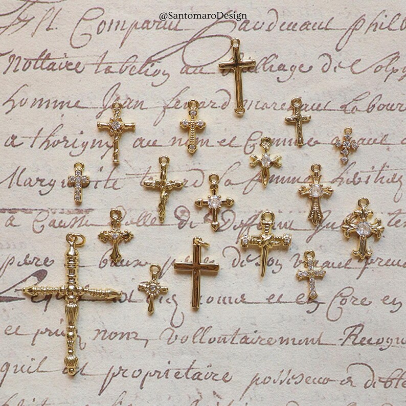 May include: A collection of gold-colored cross charms, some adorned with clear gemstones. The crosses vary in size and design, with intricate details. The background features vintage script.