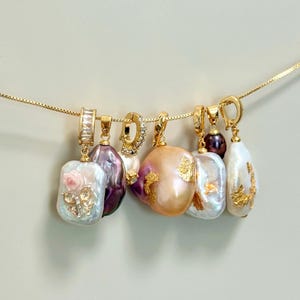 May include: A selection of gold necklaces featuring irregular pearl pendants. The pendants are in shades of white, purple, and peach, with some decorated with gold leaf and floral accents. The image includes the text "@SantomaroDesign".