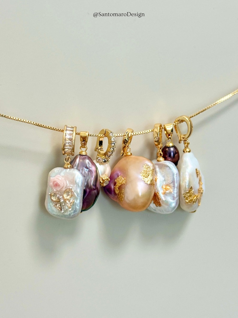 May include: A selection of gold necklaces featuring irregular pearl pendants. The pendants are in shades of white, purple, and peach, with some decorated with gold leaf and floral accents. The image includes the text "@SantomaroDesign".