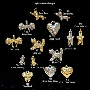 May include: A collection of small, metallic charms in gold and silver tones. The charms include animal shapes like dogs, cats, and rabbits, along with bows, hearts, and a bell. Each charm is numbered and labeled with its description.