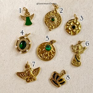 Pu&ograve; includere: Una collezione di ciondoli color oro con vari design. I ciondoli includono un angelo con un vestito in smalto verde, un motivo a raggiera con una pietra verde e una corona. Alcuni ciondoli presentano pietre preziose verdi e dettagli di perle.