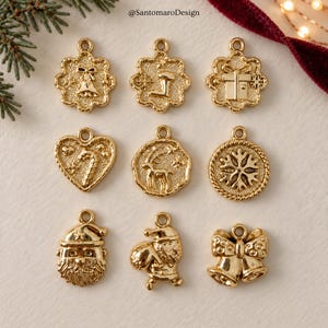 Può includere: Una collezione di nove ciondoli in metallo color oro con motivi natalizi, tra cui una campana, una calza, un regalo, un bastoncino di zucchero, una renna, un fiocco di neve, un volto di Babbo Natale, un Babbo Natale e due campanelle.