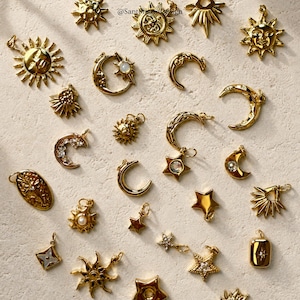 Può includere: Una collezione di ciondoli celesti color oro, tra cui soli, lune e stelle. Alcuni ciondoli presentano dettagli intricati e pietre preziose. I ciondoli sono disposti su una superficie dai toni neutri.