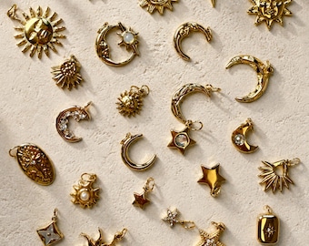 Puede incluir: Una colección de colgantes celestiales dorados, que incluyen soles, lunas y estrellas. Algunos colgantes presentan detalles intrincados y piedras preciosas. Los colgantes están dispuestos sobre una superficie de tono neutro.