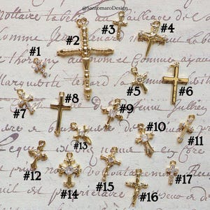 May include: A collection of gold-colored cross charms, each with a unique design. Some crosses feature sparkling embellishments, while others have a simple, elegant look. The charms are numbered for easy selection, perfect for jewelry making or religious crafts.