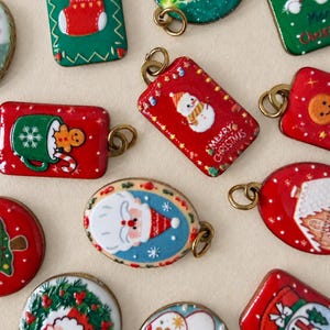 Può includere: Una collezione di piccoli ciondoli in smalto colorato con temi natalizi, tra cui Babbo Natale, pupazzi di neve, omini di pan di zenzero, calze e ghirlande. Ogni ciondolo è dotato di un anellino in metallo dorato per essere appeso come gioiello.