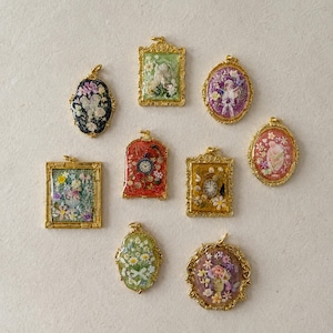 May include: Nine decorative pendants with gold-toned frames, featuring various floral, clock, and figure motifs encased in resin. The collection includes rectangular, oval, and arched shapes with colourful backgrounds. Text @SantomaroDesign is visible.