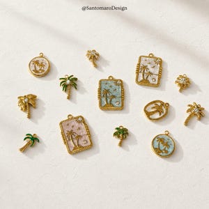 Puede incluir: Colección de colgantes dorados con diseños de palmeras. Algunos colgantes tienen forma rectangular o circular con un fondo pintado en tonos azules, rosas y blancos. Varios colgantes están adornados con pequeños cristales.