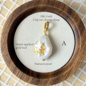 May include: A natural pearl pendant with hand-applied gold leaf accents. The pendant has an 18K gold clip-on charm clasp. The image also includes the text "@SantomaroDesign", "18K Gold Clip-on charm clasp", "Hand-applied gold leaf", "A", and "Natural pearl".