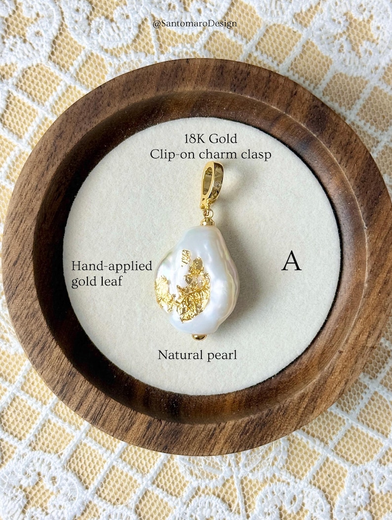 May include: A natural pearl pendant with hand-applied gold leaf accents. The pendant has an 18K gold clip-on charm clasp. The image also includes the text "@SantomaroDesign", "18K Gold Clip-on charm clasp", "Hand-applied gold leaf", "A", and "Natural pearl".