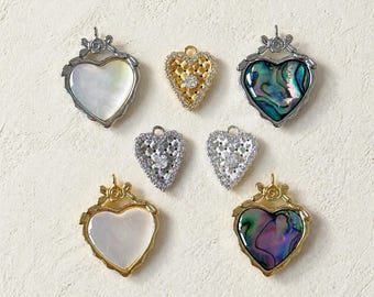 Può includere: Una collezione di ciondoli a forma di cuore in vari design. Alcuni presentano dettagli in madreperla, abalone o cristallo, mentre altri sono dorati o argentati. Adatti per la creazione di gioielli.