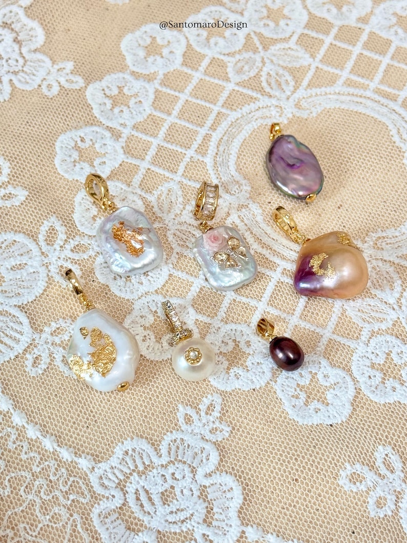 May include: A selection of pearl pendants with gold-coloured detailing. The pearls are in various shapes and colours, including white, pink, purple, and brown. Some pendants have additional embellishments. The image includes the text "@SantomaroDesign".