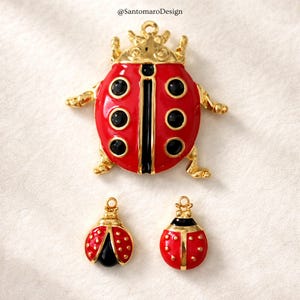 Può includere: Tre ciondoli a tema coccinella in rosso, nero e oro. Il ciondolo più grande è una coccinella dettagliata con una corona. I ciondoli più piccoli hanno un design simile, con smalto rosso e dettagli neri. I ciondoli sono probabilmente per la creazione di gioielli.