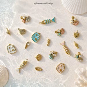 Può includere: Una collezione di ciondoli dorati con disegni a tema oceanico, tra cui conchiglie, pesci, cavallucci marini e stelle marine. Alcuni ciondoli presentano perle e accenti di smalto colorato nei toni del blu, del rosa e del bianco. I ciondoli sono sparsi su una superficie chiara.