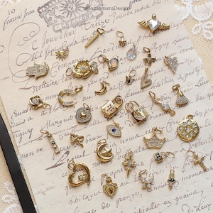 May include: A collection of gold-toned charms with various designs, including hearts, locks, stars, and crowns. Some charms are embellished with clear crystals. The charms are displayed on a vintage paper background.