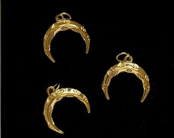 May include: Three gold-colored crescent moon pendants with intricate etched designs. Each pendant has a small loop at the top for attaching to a chain or other jewelry component. The pendants are displayed against a black background.