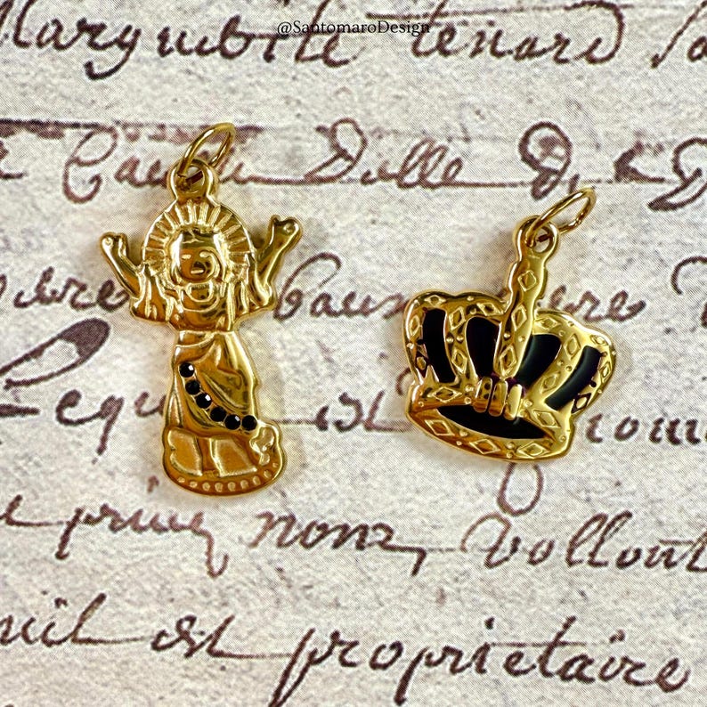 Pu&ograve; includere: Due ciondoli color oro. Uno &egrave; una figura stilizzata con le braccia tese e dettagli neri. L'altro &egrave; una corona con dettagli in smalto nero. Entrambi i ciondoli hanno un anello per una catena.