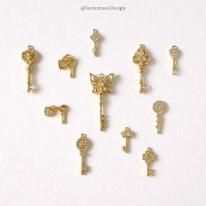 Pode incluir: Uma coleção de pingentes de chave dourados com vários designs, incluindo uma borboleta, uma coroa e padrões florais. Algumas chaves são adornadas com pequenos enfeites brilhantes. A imagem está em um fundo branco.