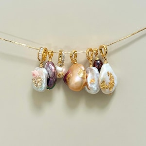 May include: Seven gold-toned pendant necklaces with baroque pearls. Each pendant has a unique pearl shape and colour, some with gold leaf accents. The necklaces are suspended against a neutral background.
