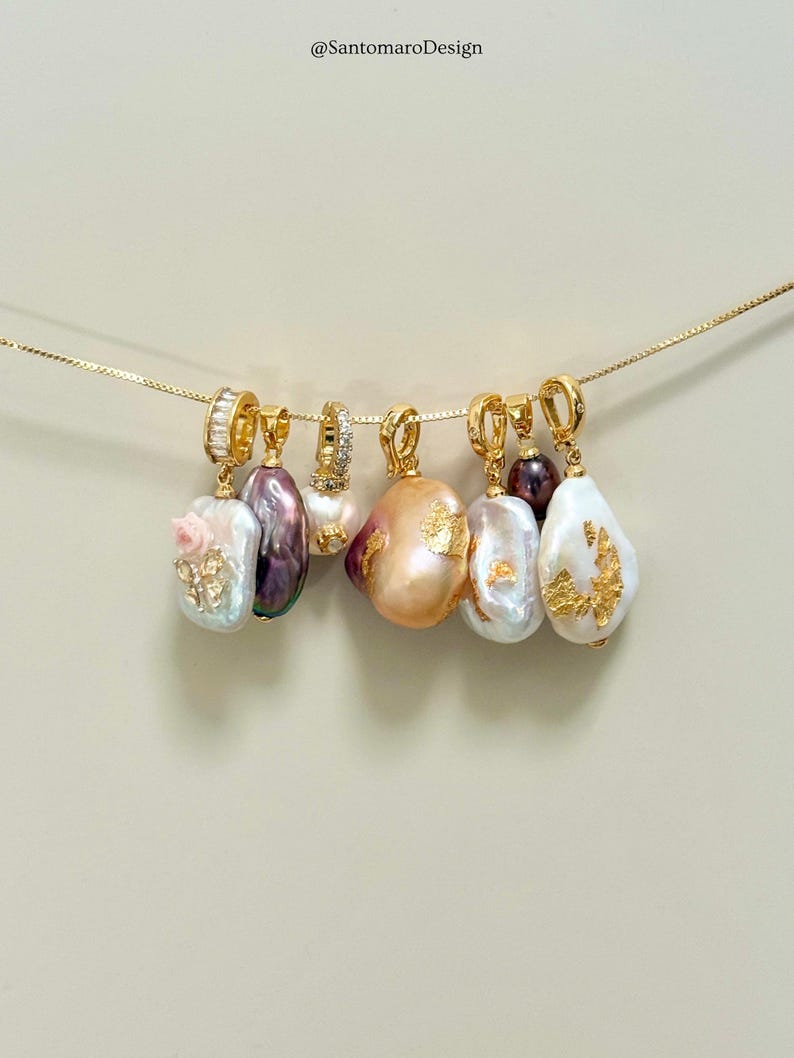 May include: Seven gold-toned pendant necklaces with baroque pearls. Each pendant has a unique pearl shape and colour, some with gold leaf accents. The necklaces are suspended against a neutral background.