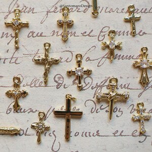 May include: A collection of gold-colored cross charms, some adorned with clear gemstones. The crosses vary in design, including ornate and simple styles. The charms are likely for jewelry making or religious-themed crafts.