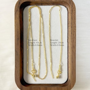 May include: A gold-colored necklace and bracelet set displayed in a wooden tray. The necklace is 45cm long and the bracelet is 20cm long, both with a width of 0.9mm. The text on the image reads "Necklace Length: 45cm Width:0.9mm" and "Bracelet Length: 20cm Width:0.9mm".