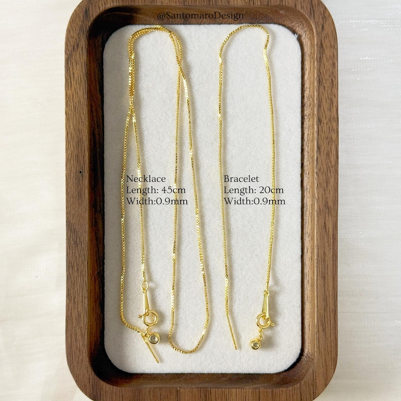 May include: A gold-colored necklace and bracelet set displayed in a wooden tray. The necklace is 45cm long and the bracelet is 20cm long, both with a width of 0.9mm. The text on the image reads "Necklace Length: 45cm Width:0.9mm" and "Bracelet Length: 20cm Width:0.9mm".