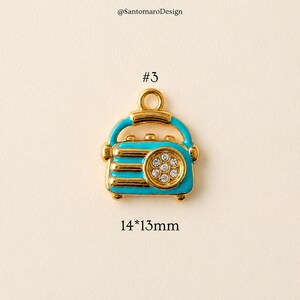 May include: A gold-toned charm in the shape of a vintage radio, with a turquoise blue body and gold accents. The radio has a circular design with clear crystals and measures 14mm x 13mm.