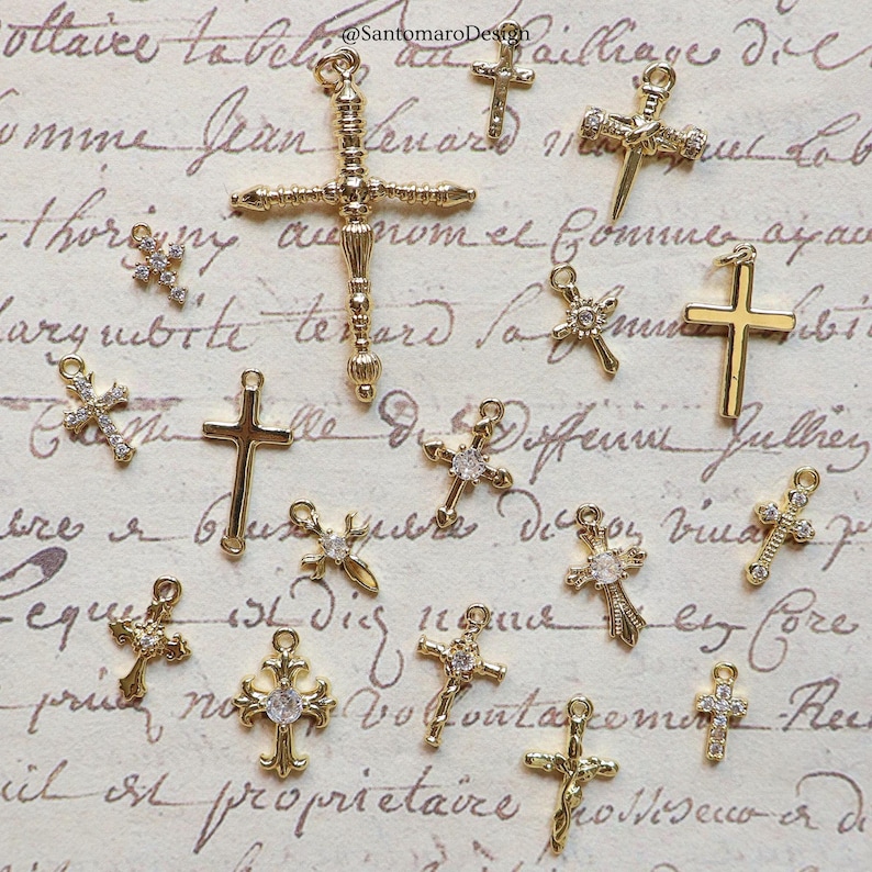 May include: A collection of gold-colored cross charms, some adorned with clear crystals. The crosses vary in design, with some featuring ornate detailing and others a simpler, classic shape. The charms are displayed on a vintage-style paper background.
