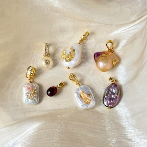 May include: A selection of gold-plated pendants featuring pearls and gemstones. The pendants showcase baroque pearls with gold detailing, a pearl with a diamond-set bale, and a rectangular pendant with a floral design.