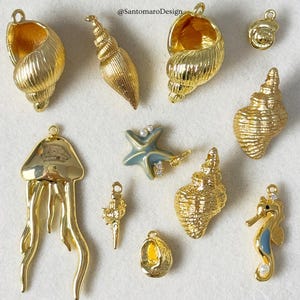 Può includere: Una collezione di ciondoli a forma di conchiglia dorata, tra cui conchiglie, una stella marina, un cavalluccio marino e una medusa. Alcuni ciondoli hanno accenti di perle e cristalli. I ciondoli sono progettati per la creazione di gioielli o l'artigianato.