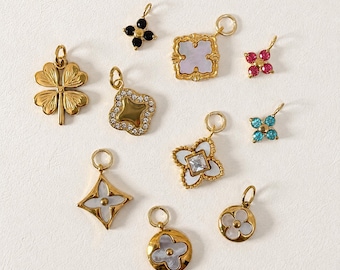May include: A collection of gold-toned charms in various shapes, including a four-leaf clover, a square with a crystal border, and a round charm with a flower design. Some charms feature gemstones or mother-of-pearl inlays. The text "@SantomaroDesign" is visible.