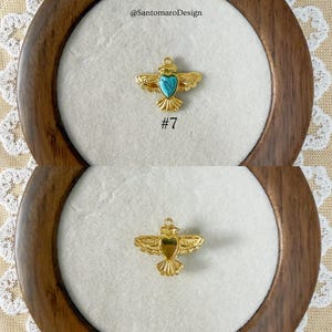 Peut inclure: Pendentif dor&eacute; en forme d'oiseau avec un c&oelig;ur turquoise au centre. Le pendentif est pr&eacute;sent&eacute; sur une surface blanche dans un cadre en bois. Le num&eacute;ro "#7" est en dessous. Le texte "@SantomaroDesign" est en haut.