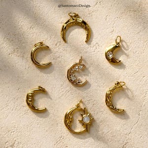 Peut inclure: Une collection de breloques en forme de croissant de lune dorées. Certaines breloques présentent des motifs complexes, tandis que d'autres comportent des cristaux incrustés ou un motif de soleil avec une pierre centrale. Les breloques sont présentées sur une surface texturée et claire.