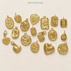 May include: A selection of gold-coloured pendants and charms with diverse designs. The charms feature floral, heart, and cameo motifs. Some pendants include a small gemstone. The charms are arranged on a light-coloured surface.