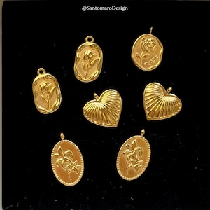 Può includere: Una collezione di ciondoli color oro con disegni floreali e a forma di cuore. I ciondoli includono una rosa, un tulipano e un giglio. I ciondoli sono di varie forme, tra cui ovale, rettangolare e a forma di cuore. I ciondoli sono esposti su una superficie nera.