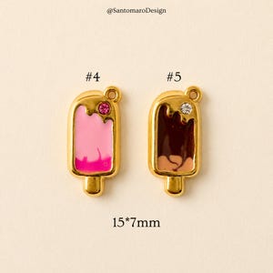 May include: Two gold-toned popsicle charms, each with a different color scheme. One features pink and light pink enamel with a pink gem, the other has brown and tan enamel with a clear gem. The charms are 15mm x 7mm.