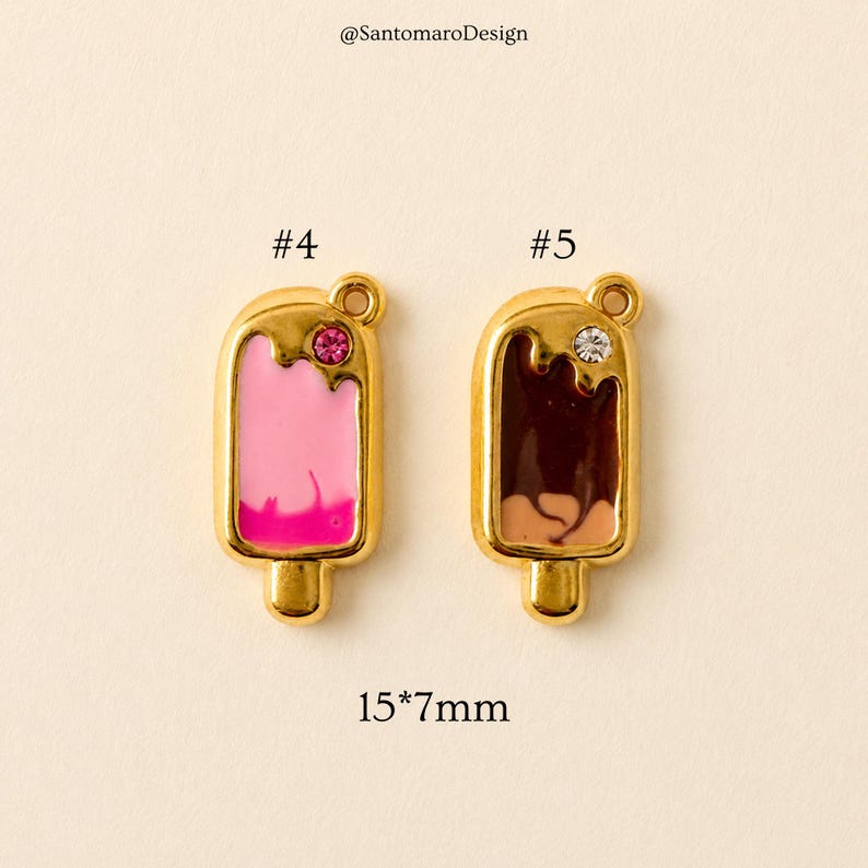 May include: Two gold-toned popsicle charms, each with a different color scheme. One features pink and light pink enamel with a pink gem, the other has brown and tan enamel with a clear gem. The charms are 15mm x 7mm.