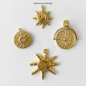 Può includere: Quattro ciondoli in metallo dorato con disegni celesti, tra cui un sole con un volto, un raggio di sole testurizzato, un sole con luna crescente e un medaglione circolare con una stella centrale. Il testo @SantomaroDesign è visibile in alto.