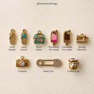 May include: A collection of gold-toned charms, including a sandal, radio, ice cream, sewing machine, camera, safety pin, and coffee cup. The charms have colorful accents and are displayed on a neutral background. The text "@SantomaroDesign" is at the top.
